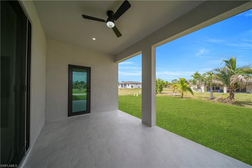 Covered patio featuring large format tile flooring, a ceiling fan, and recessed lighting, opening to a spacious lawn with palm trees