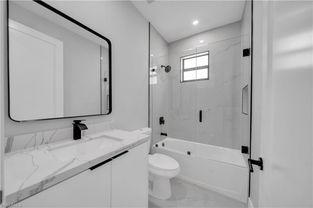 Modern bathroom featuring a single vanity with a white countertop and integrated sink, a rectangular framed mirror, a tub-shower combination with glass enclosure, white tile surround, and matte black fixtures