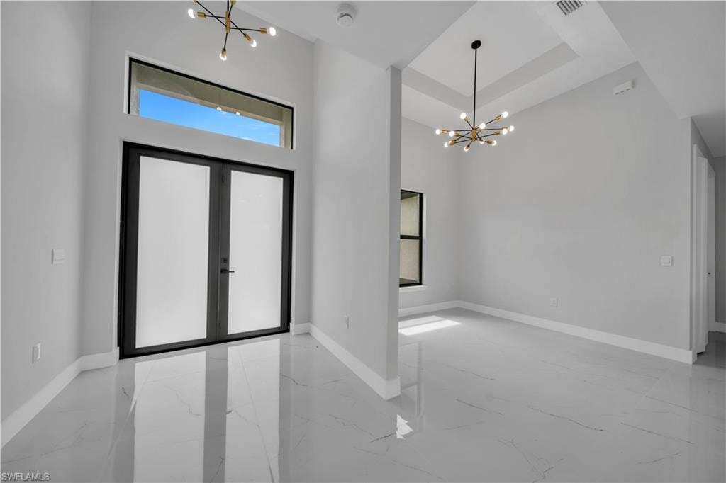 Double entry doors with transom window, polished porcelain tile flooring, and two contemporary Sputnik chandeliers
