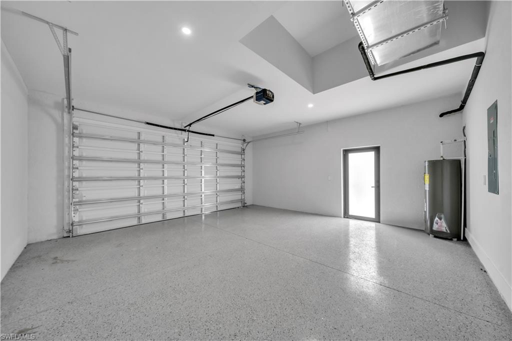 Spacious garage featuring a finished epoxy floor, an overhead garage door with an automatic opener, a frosted glass entry door, a hot water heater, and an electrical panel