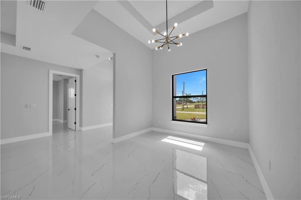 Spacious interior room featuring high ceilings with a tray ceiling detail, a modern sputnik-style chandelier, large black-framed window, and polished tile flooring with subtle veining