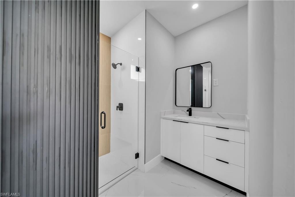 Modern bathroom with a glass-enclosed shower, white vanity with integrated sink, black framed mirror, and recessed lighting