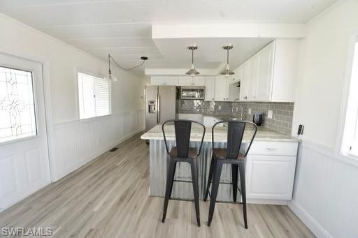 Bright kitchen featuring white cabinetry, stainless steel appliances, a light-toned countertop, and a gray subway tile backsplash