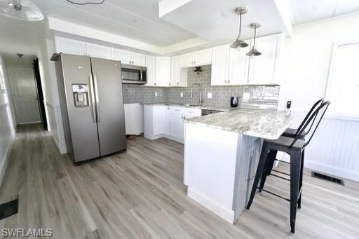 Contemporary kitchen featuring white cabinetry, a light gray tile backsplash, stainless steel appliances, a breakfast bar with stone-finish countertop, and wood-finish flooring