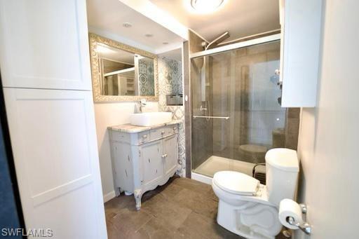 Bathroom featuring a glass-enclosed shower, a vanity with an integrated vessel sink, a decorative framed mirror, patterned wall tiling, and wood-finish flooring