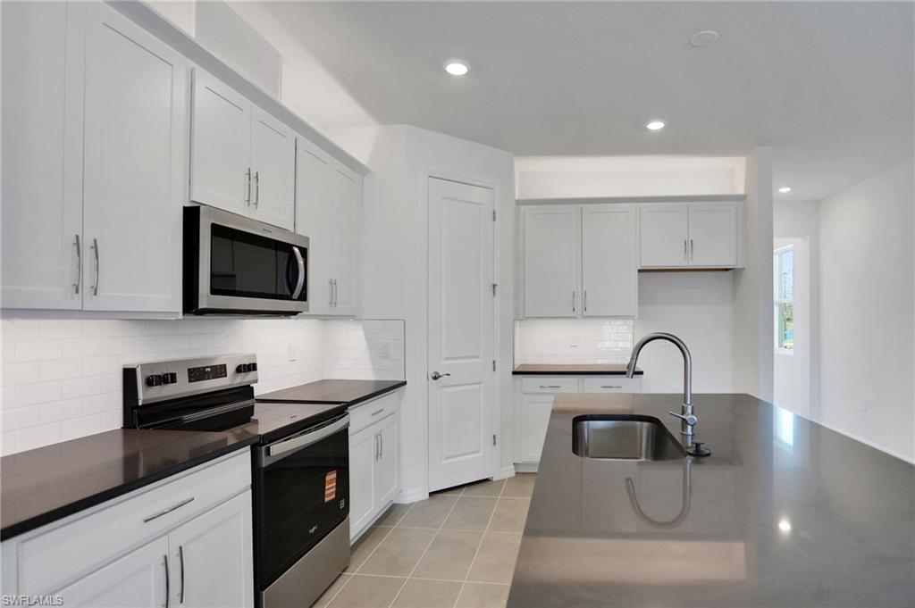Kitchen with stainless steel appliances, white cabinetry, light tile patterned flooring, recessed lighting, and dark stone countertops