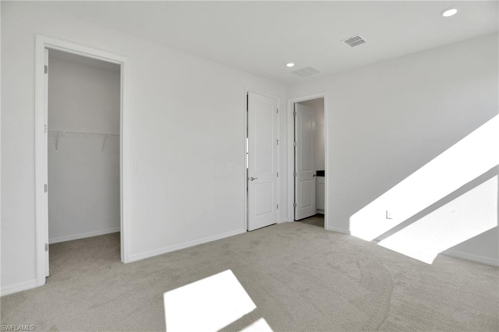 Unfurnished bedroom with a spacious closet, light colored carpet, and recessed lighting