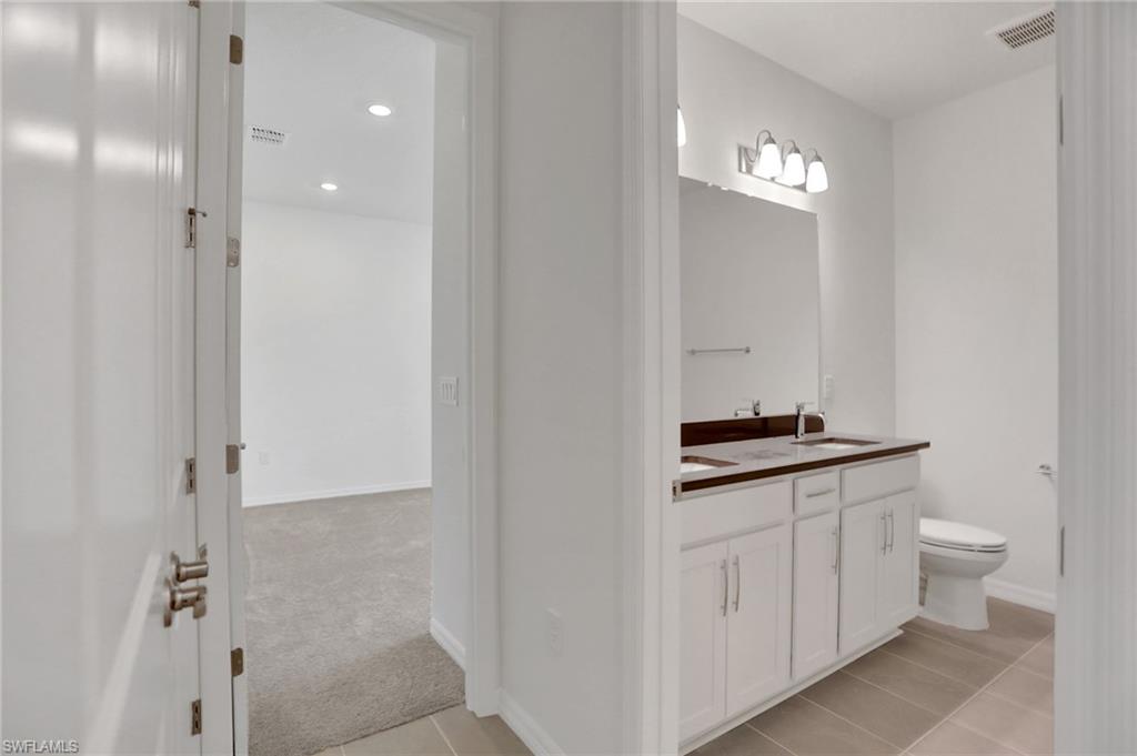 Bathroom with double vanity, light colored carpet, light tile patterned flooring, and recessed lighting