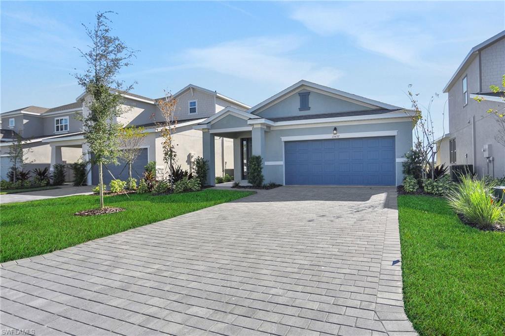 View of front of property featuring a front yard, decorative driveway, stucco siding, and a garage
