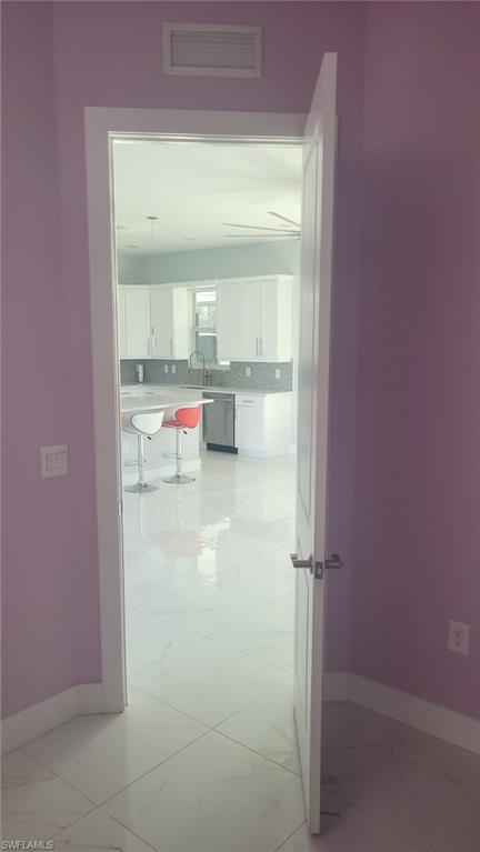 Open doorway reveals a modern kitchen featuring white shaker cabinetry, an undermount sink with a gooseneck faucet, a stainless steel appliance, and light-toned tile flooring