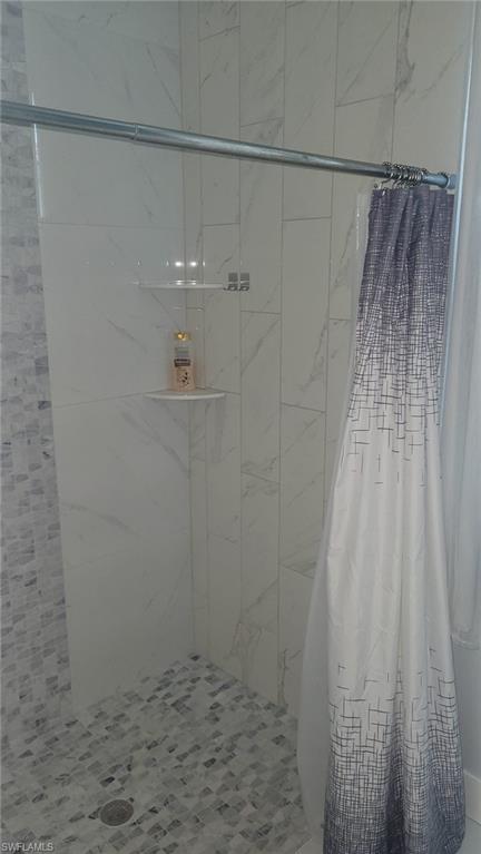 Shower stall with floor-to-ceiling white and gray veined tile, mosaic tile shower pan, and built-in corner shelving