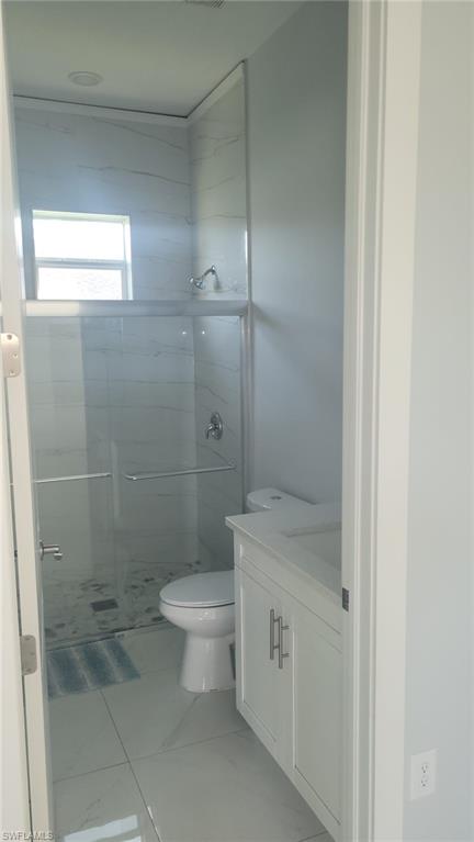 Bathroom featuring a glass-enclosed shower, white tile walls with subtle veining, a single window, a white vanity with double-door cabinetry, and a white countertop with an integrated sink