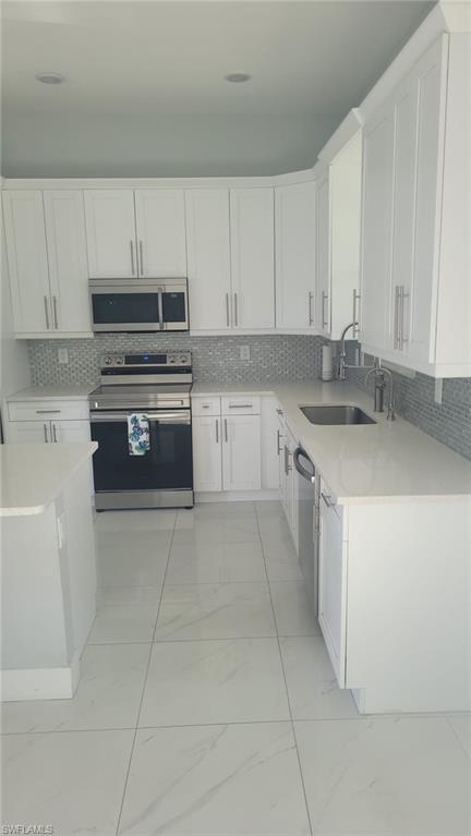 Modern kitchen featuring white shaker cabinetry, stainless steel appliances, a light-toned countertop, a gray mosaic tile backsplash, and large format floor tiling