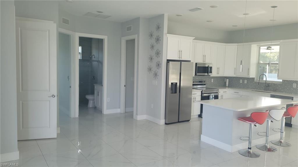 Open-concept kitchen featuring white cabinetry, stainless steel appliances, a large island with countertop seating, and a patterned tile backsplash