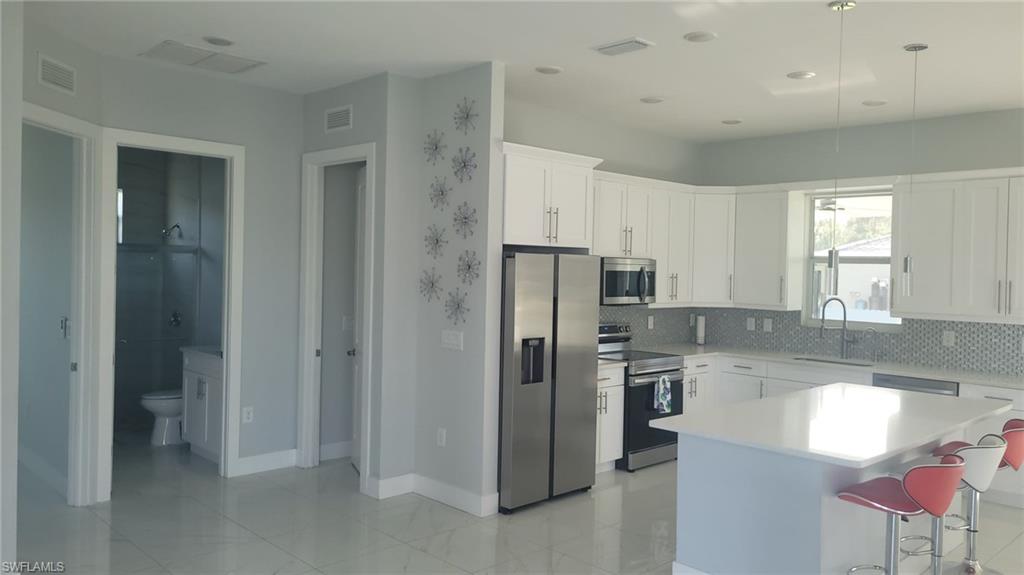 Bright kitchen featuring white shaker cabinetry, stainless steel appliances, a white island with pendant lighting, and a mosaic tile backsplash