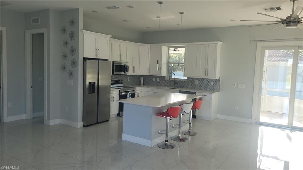 Spacious kitchen featuring white cabinetry, stainless steel appliances, a center island with countertop seating, a mosaic tile backsplash, and large format tile flooring