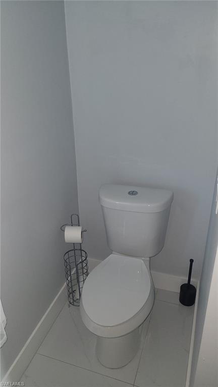 White toilet with a dual-flush mechanism, light gray wall paint, and large format floor tiling