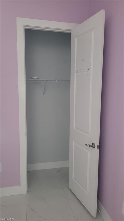 Interior closet featuring white wire shelving, a white paneled door with brushed nickel hardware, and marble-look tile flooring