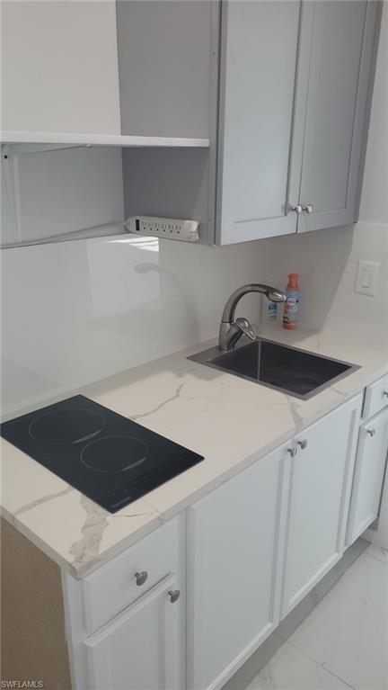Compact kitchen area featuring white shaker-style base cabinetry, light gray upper cabinetry, and a white countertop with subtle veining
