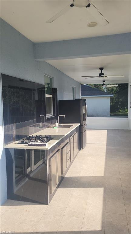 Outdoor kitchen featuring a built-in gas cooktop, integrated sink with faucet, ample counter space, and enclosed cabinetry