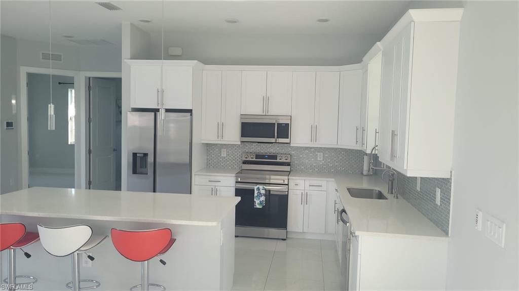 Modern kitchen featuring white cabinetry, stainless steel appliances, a mosaic tile backsplash, a large island with a light-toned countertop, and recessed lighting