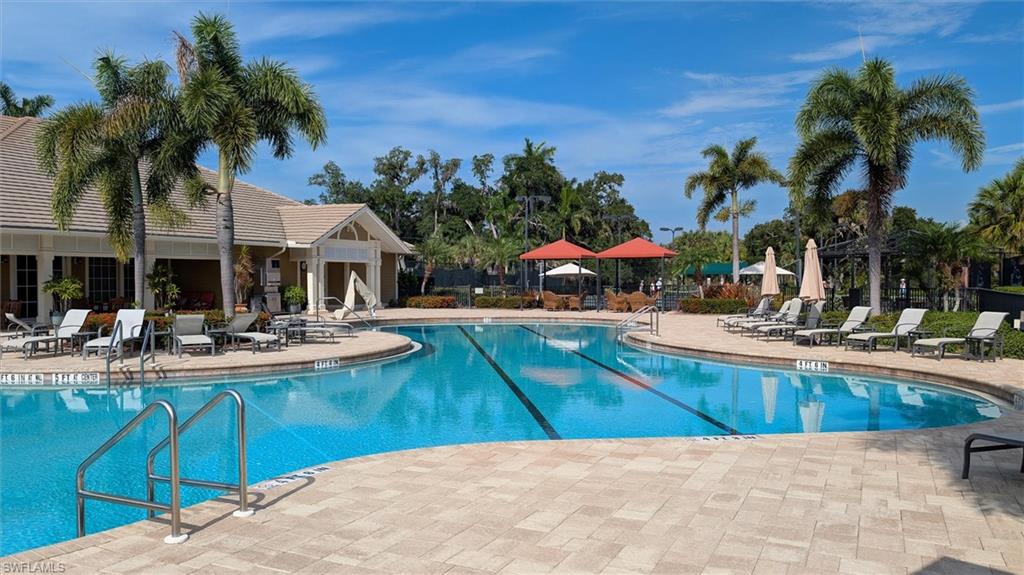 Resort-style swimming pool featuring a curved design, paved sundeck, and lush tropical landscaping