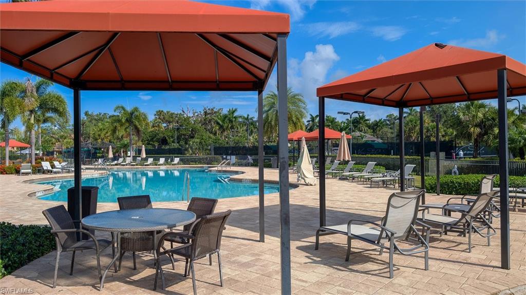 Resort-style pool area featuring a free-form swimming pool, paver deck, covered seating areas with outdoor furniture, and mature palm tree landscaping