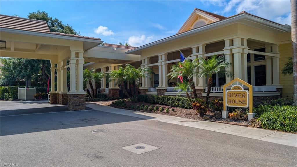 Building facade featuring a covered entry, stucco exterior, tiled roof, decorative columns with stone bases, and mature landscaping