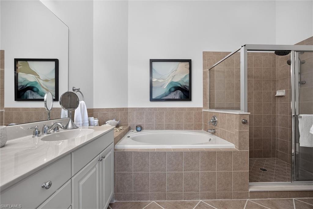 Bathroom featuring a built-in jetted tub, a glass-enclosed shower, a double vanity with a light-toned countertop, and tiled flooring