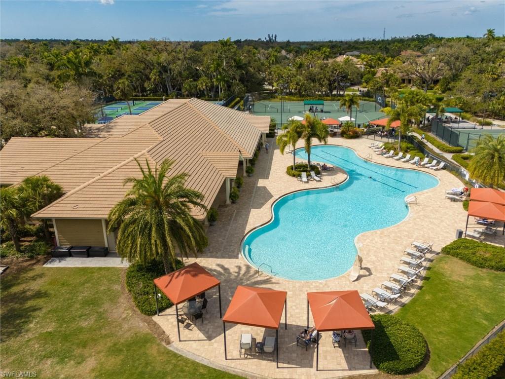 Resort-style pool area featuring a freeform swimming pool, extensive paved deck, and multiple shaded seating areas