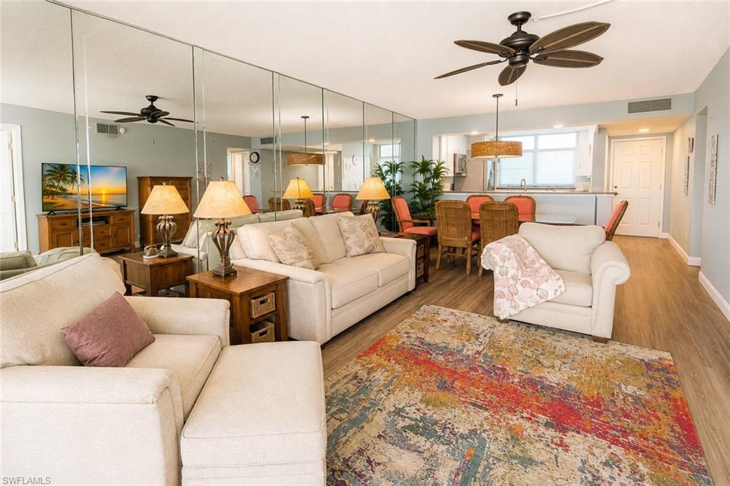 Open-concept living space featuring wood-finish flooring, a ceiling fan, and a mirrored accent wall
