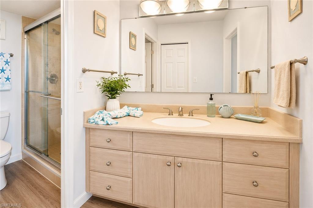 Bathroom featuring a light-toned vanity with an integrated sink and countertop, a large wall-mounted mirror, and a glass-enclosed shower with tiled walls