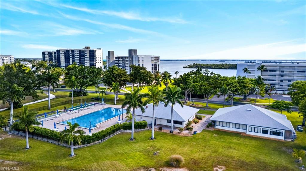 Community outdoor pool with surrounding patio space and tropical landscaping, complemented by adjacent recreational buildings and water views