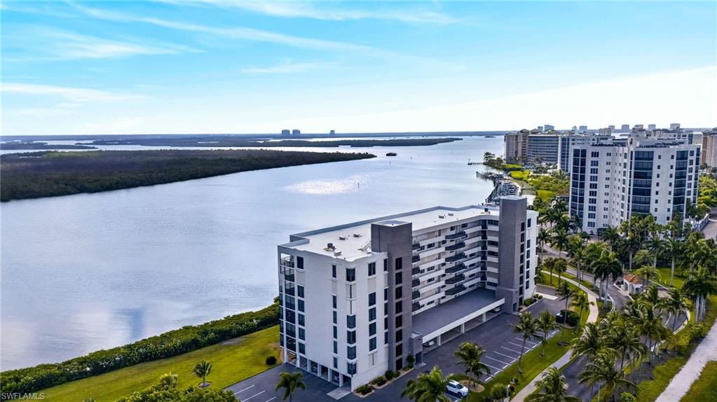 Waterfront condominium building featuring multiple balconies, covered parking, and landscaping with palm trees