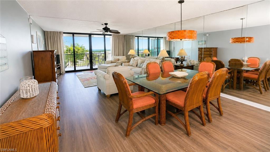 Open-concept living and dining area featuring wood-finish flooring, full-length wall mirrors, and direct balcony access with elevated exterior views
