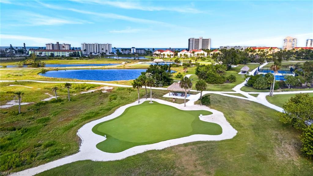 Putting green with sand trap, surrounded by green spaces, paved pathways, and mature palm trees