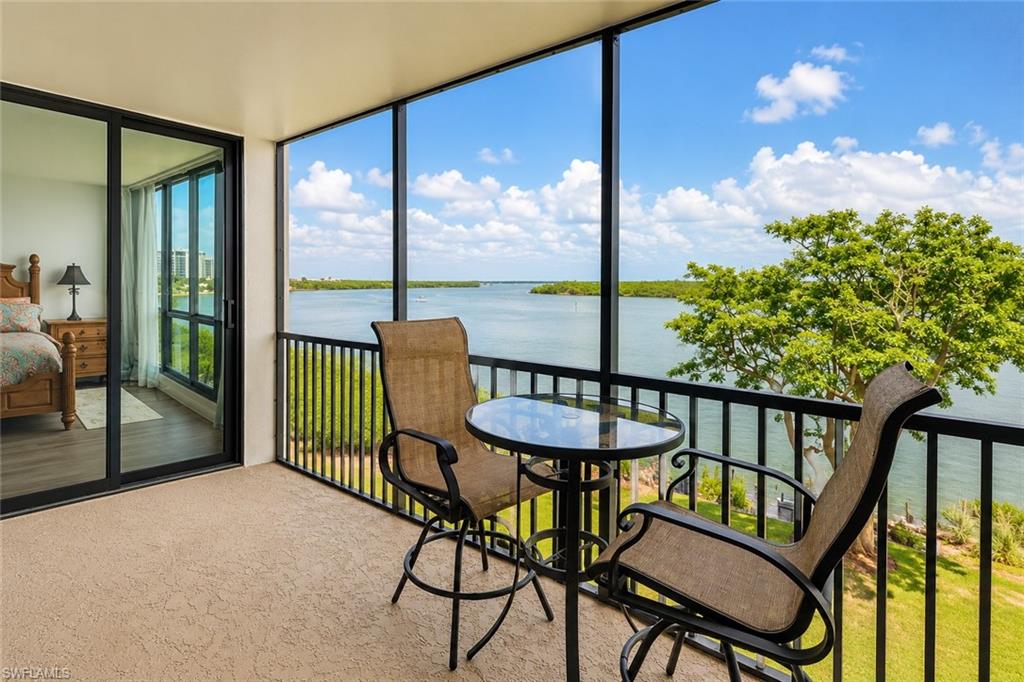 Screened balcony featuring textured flooring, black metal railing, and expansive water frontage with natural landscaping