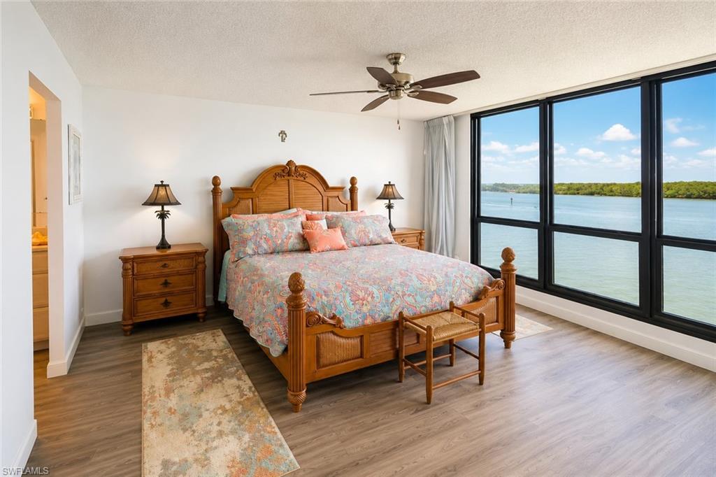 Expansive window wall with water scenery, wood-finish flooring, ceiling fan, and white walls
