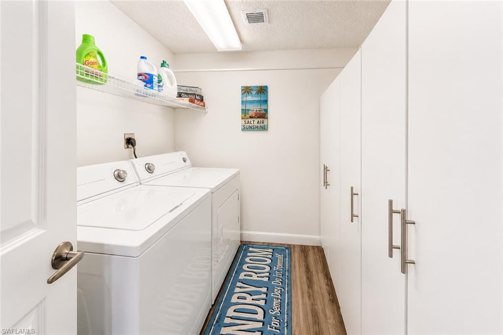 Dedicated laundry area featuring a washer and dryer, wood-finish flooring, built-in white cabinetry with brushed nickel pulls, a wire storage shelf, and recessed lighting