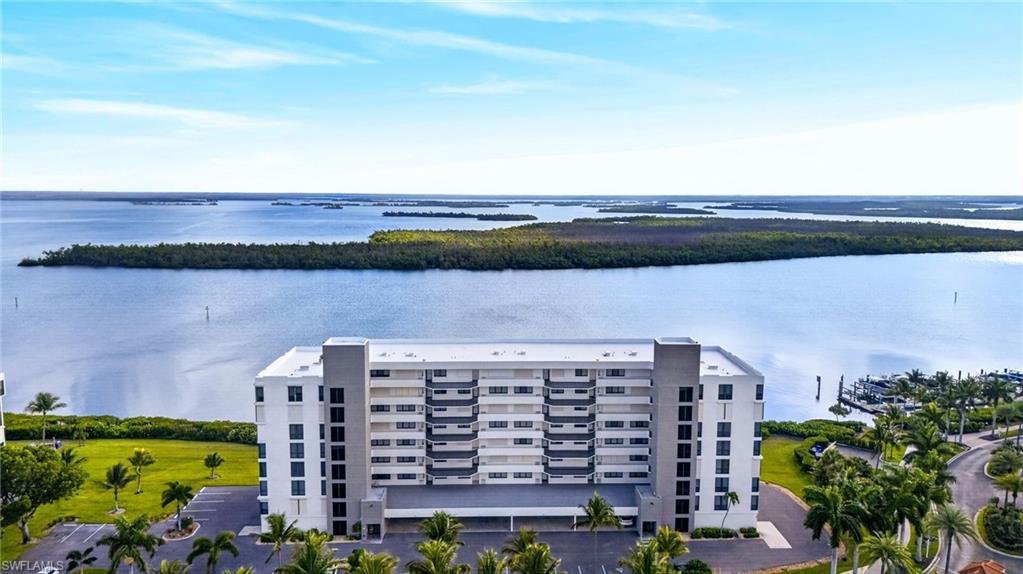Modern multi-story building featuring extensive water frontage, a private marina, mature palm trees, and manicured green spaces