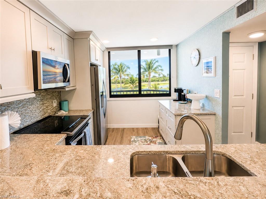 Kitchen featuring stone countertops, stainless steel appliances, white cabinetry, and a window with a tropical landscape beyond