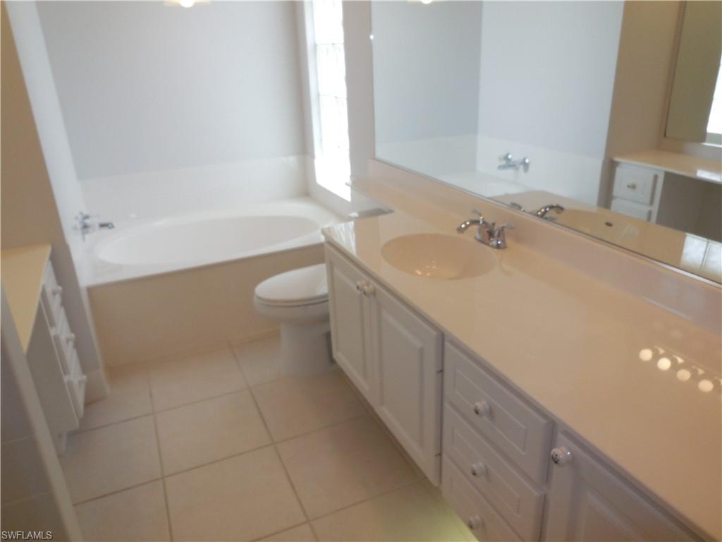 Bathroom featuring a built-in tub, a vanity with an integrated sink and white cabinetry, a long wall-mounted mirror, and tile flooring