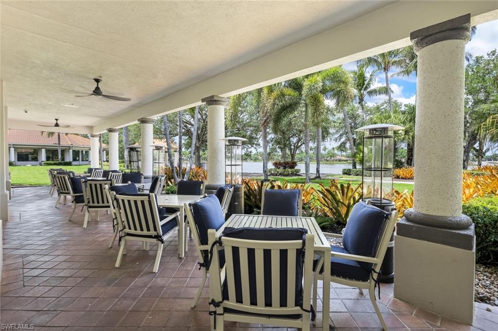 Expansive covered patio featuring a terracotta tile floor, multiple ceiling fans, decorative columns, and abundant landscaping with palm trees