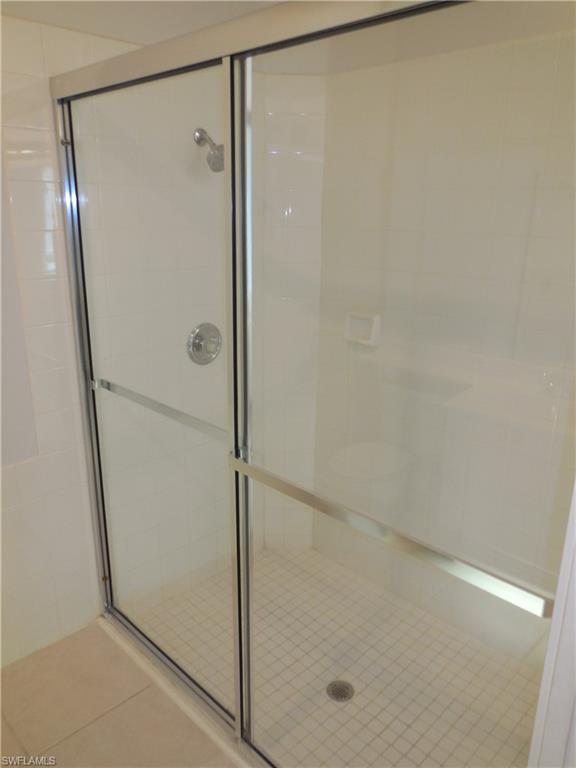 Glass-enclosed shower with a chrome shower head and handle, white tile walls, and a white mosaic tile floor