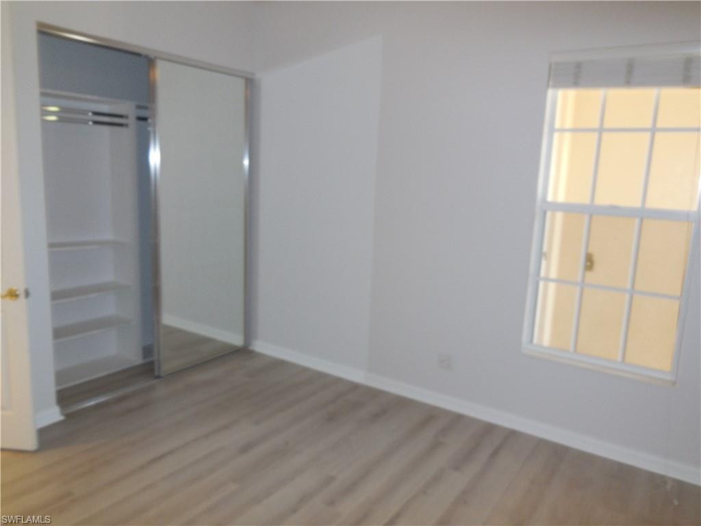 Bedroom featuring light wood-finish flooring, white baseboards, and a window with horizontal blinds