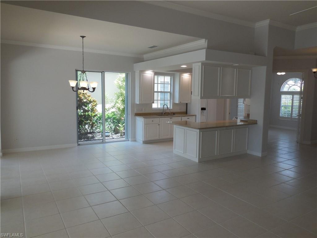 Spacious interior featuring neutral tile flooring, white kitchen cabinetry, a kitchen island with a stone countertop, a chandelier, and sliding glass doors to exterior landscaping