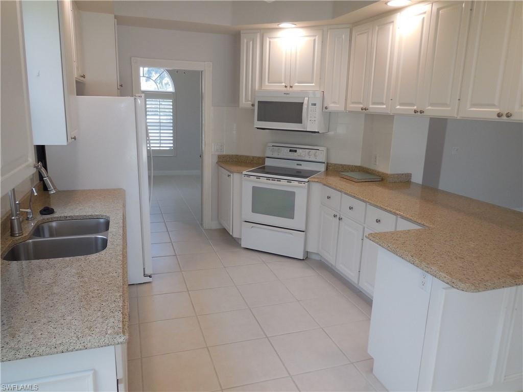 Bright kitchen featuring white cabinetry, light granite-style countertops, and white tile flooring