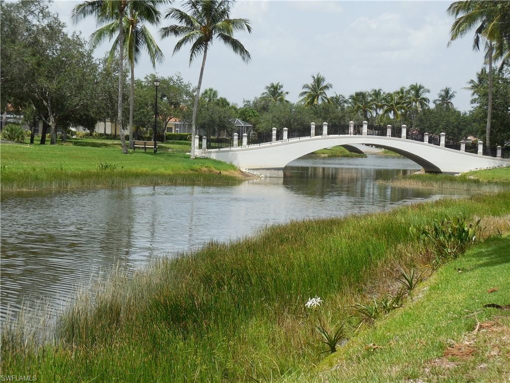 Arched pedestrian bridge spanning a tranquil waterway, bordered by lush green landscaping and mature palm trees