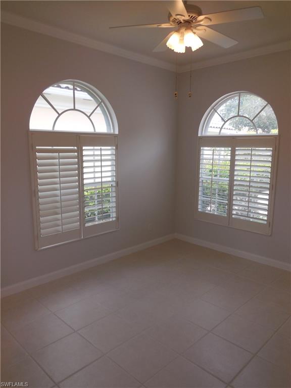 Interior space featuring two arch-top windows with plantation shutters, tile flooring, crown molding, and a ceiling fan with integrated lighting