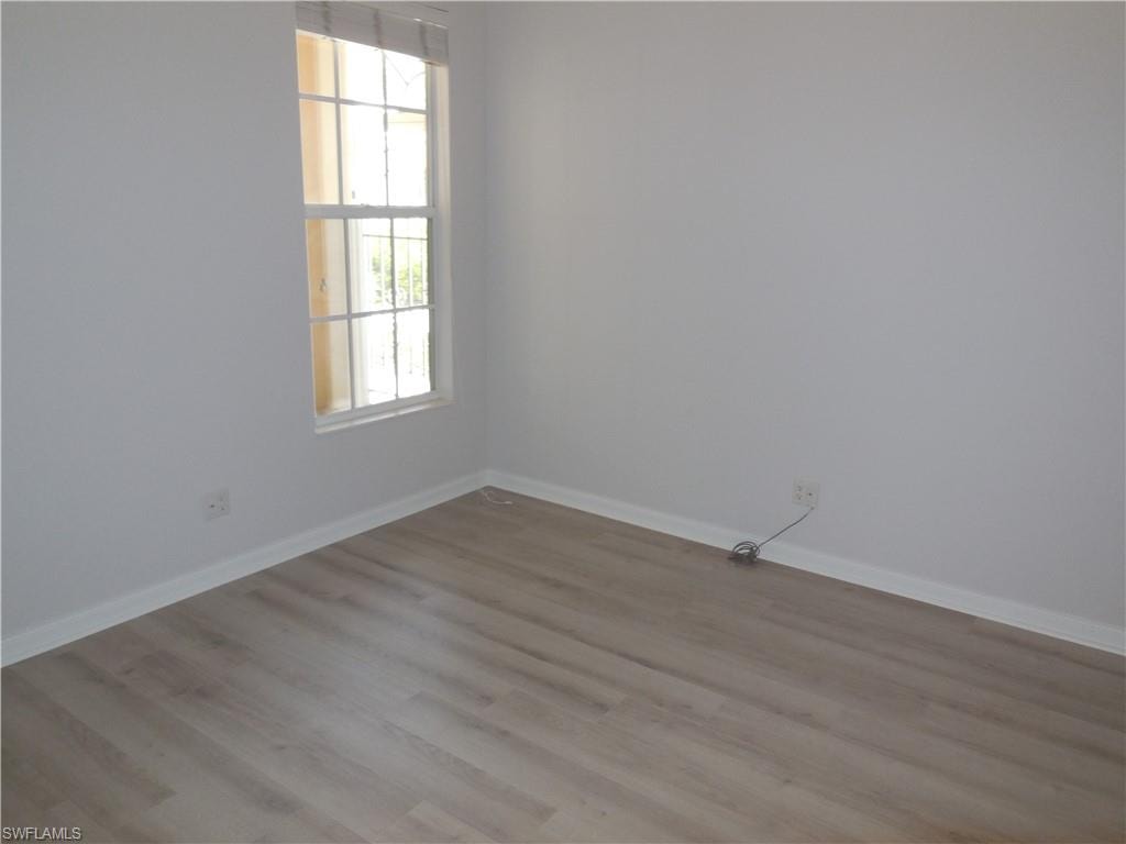 Light-filled room featuring wood-finish flooring, white baseboards, and a double-hung window with grilles